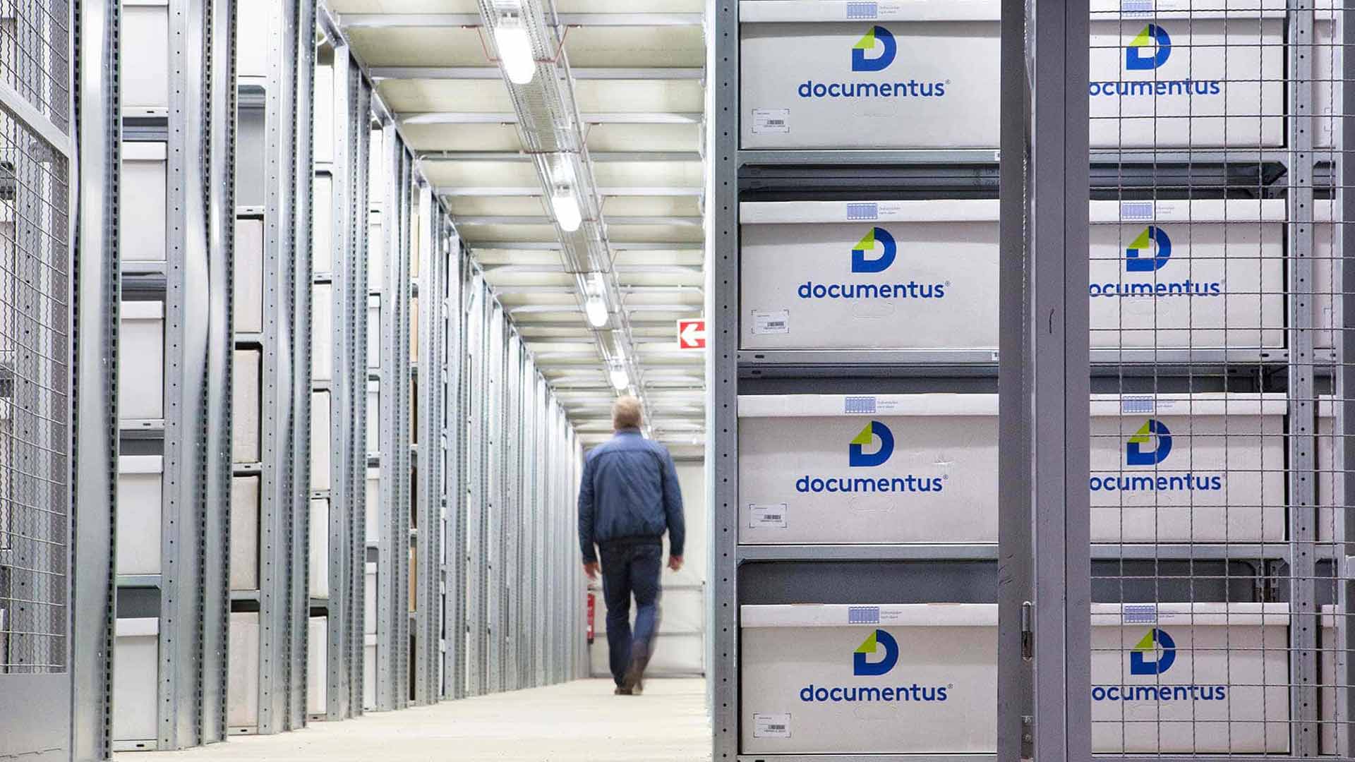 Eine Person geht durch einen Lagerraum voller weißer Kisten mit dem Logo "documentus".